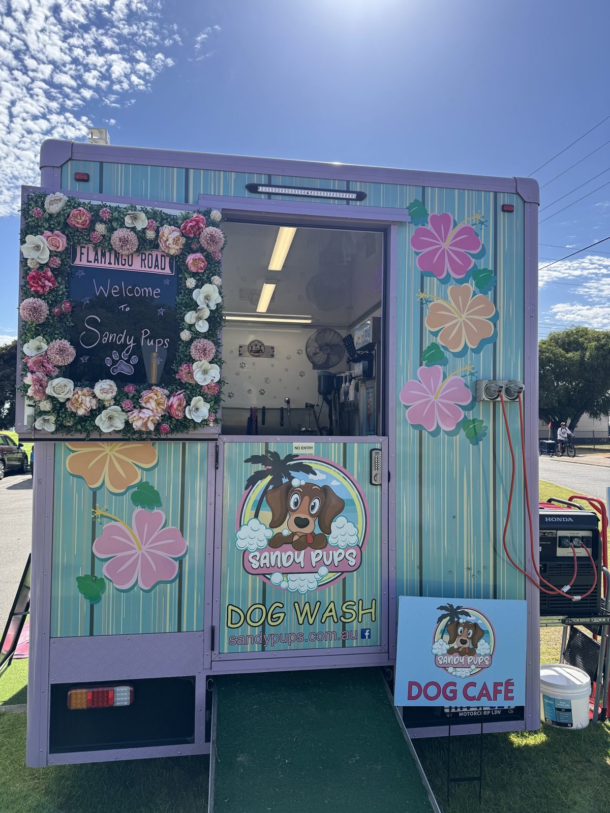 The entrance to the Sandy Pups trailer with a floral welcome board, hibiscus decals and a Dog Café sign